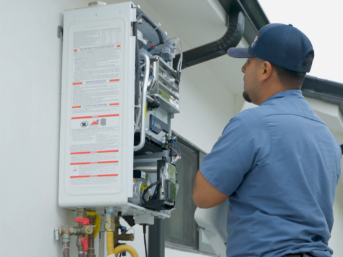 A Monkey Wrench technician is visually inspecting the inside of a tankless water heater.