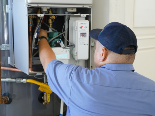 The image shows a Monkey Wrench technician checking the panel of a hybrid hot water heater.