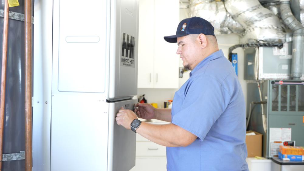 The image shows a Monkey Wrench technician removing the panel of a hybrid water heater from Noritz.