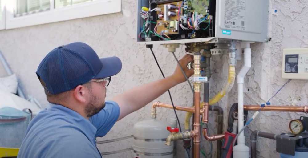 A Monkey Wrench technician inspecting the connections of a tankless water heater.