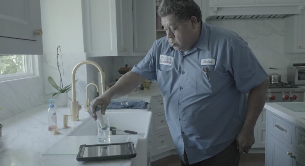 The image shows a Monkey Wrench technician testing out the hardness of water inside a home. 