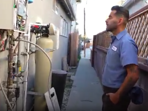 The image shows a Monkey Wrench technician inspecting a tankless water heater flush.