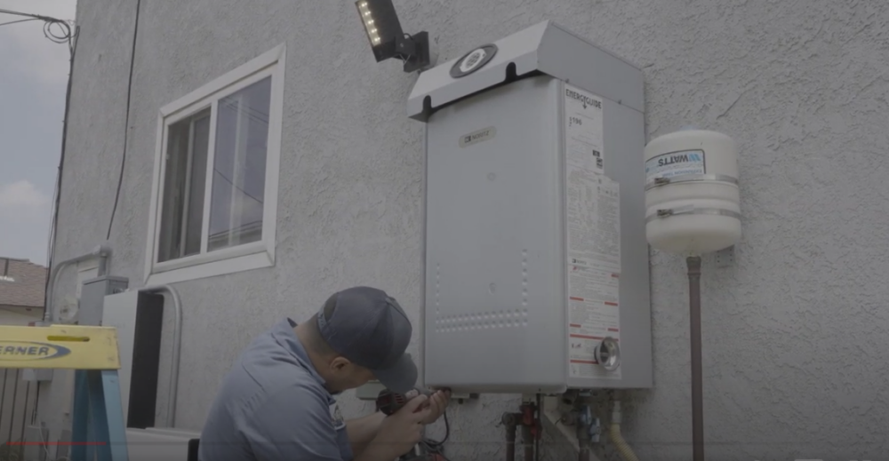 The image shows a technician working on a Noritz tankless water heater.