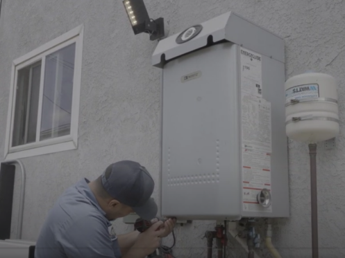 The image shows a technician working on a Noritz tankless water heater.