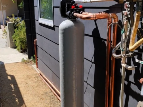 The image shows a whole-house water filtration system installed outside a home.