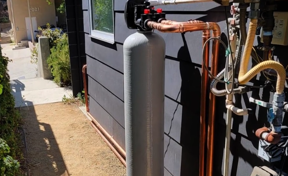 The image shows a whole-house water filtration system installed outside a home. 