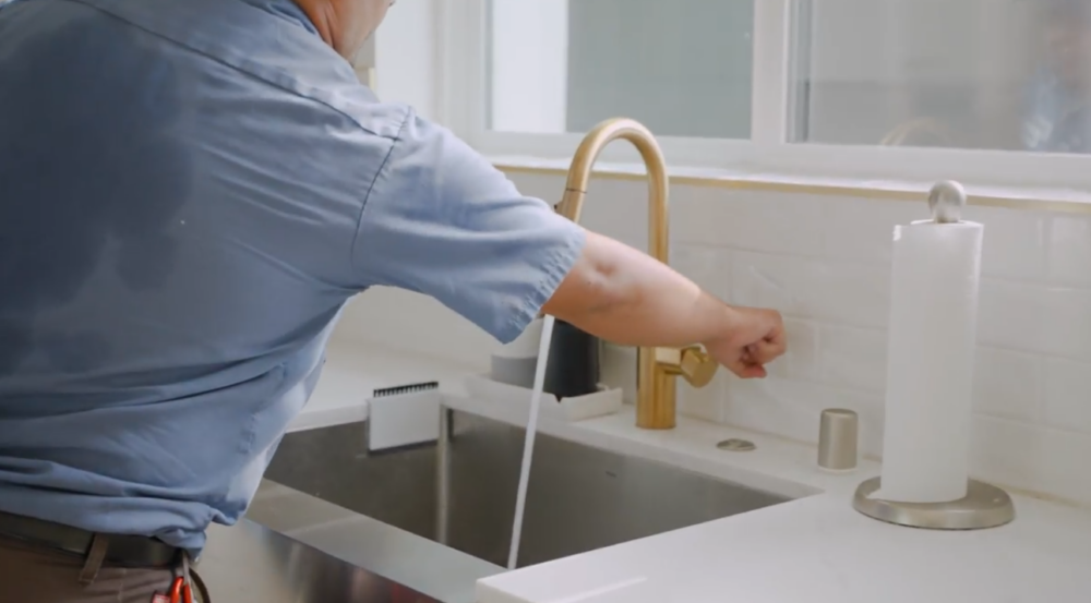 A Monkey Wrench technician is turning on a kitchen sink faucet to inspect the flow rate.