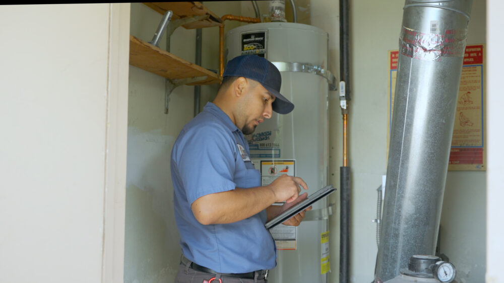 A Monkey Wrench next to a tank-style water heater going over their notes.