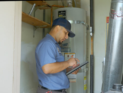 A Monkey Wrench next to a tank-style water heater going over their notes.